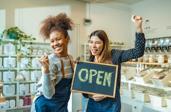 Young Woman Owner in Apron Selling Superfoods in Zero Waste Shop. .Small business: Happy owner of a cafe showing open sign.