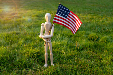 Independence day USA. Veterans day USA. Memorial day concept. Wooden mannequin with American flag on green grass background