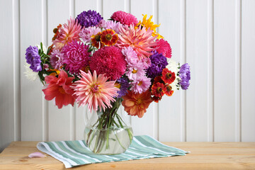 A bouquet of autumn garden flowers in a glass jug on the table. Asters, dahlias and chrysanthemums.