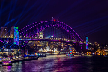 Fototapeta na wymiar 冬のシドニーのイベント・ビビッドシドニーで見た、紫にライトアップされるハーバーブリッジと周辺の夜景