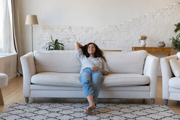 Latina woman daydream relax on sofa at home, housewife accomplish household chores reduces...