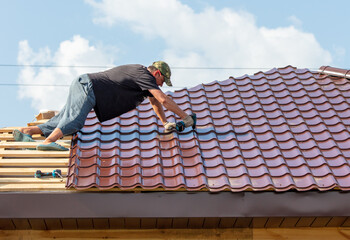 Workers install metal roofing on the wooden roof of a house.