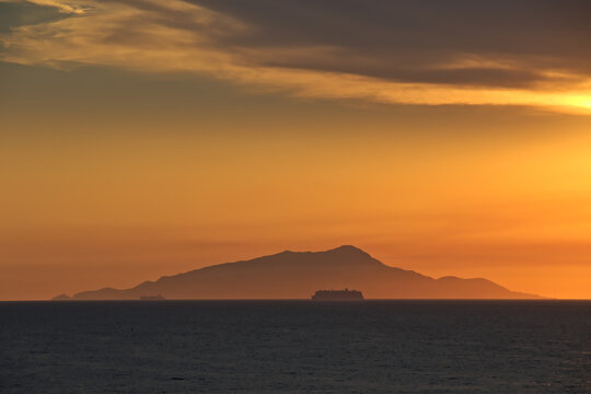 Cruise passengers ship silhouette passing before Ischia mountain in the far-off, in the Gulf of Naples, at golden hour.