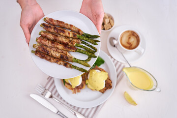Tasty eggs Benedict, hollandaise sauce and aspargus covered with bacon