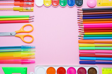 School stationery colorful paint pencils and pens on pink background in form of a frame, the concept of back to school