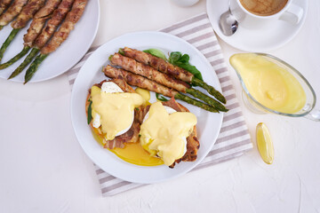 Tasty eggs Benedict, hollandaise sauce and aspargus covered with bacon