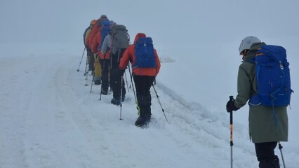 trip to mountain, hikers are walking up over snowed slope, backpacking and alpinism in snowstorm