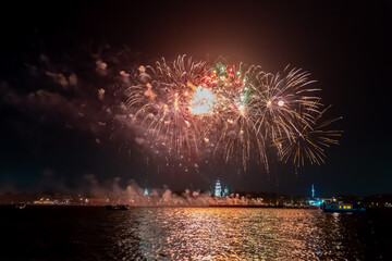 Festive fireworks in the dark sky with reflection in the water of the river at night
