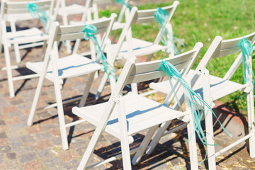 Close-up of white armchairs with turquoise bow. sunny day