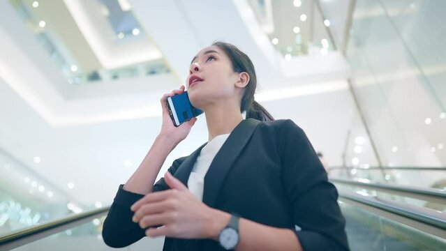 Beautiful asian woman in black suit picking up phone receiving a good news on smartphone. Low angle shot young woman a celebrating successful moment of career employment, hunting a job of dream.