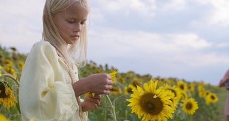 Beautiful young girl enjoying nature on the field of sunflowers at sunset. Freedom concept. Happy sisters outdoors. Harvest. Childhood. Country life.