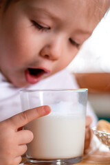 Selective focus of glass with milk on the table. Close-up of glass of milk in the hands of a cute girl in the blurry child background