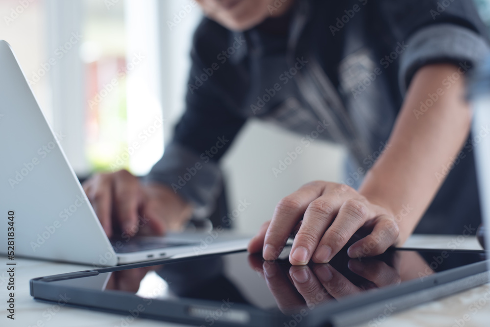 Poster closeup of business man working on laptop computer and using digital tablet pc on table at home offi