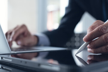 Fototapeta premium Businessman hand with stylus pen signing e-document on digital tablet, working on laptop computer at office, e-signing, electronic signature, close up