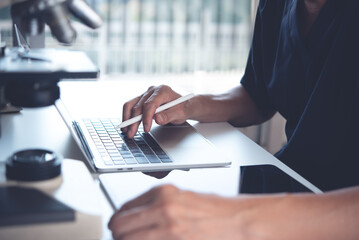 Scientist working on laptop computer and using digital tablet with microscope. Doctor or technician recording lab test on tablet pc in hospital laboratory