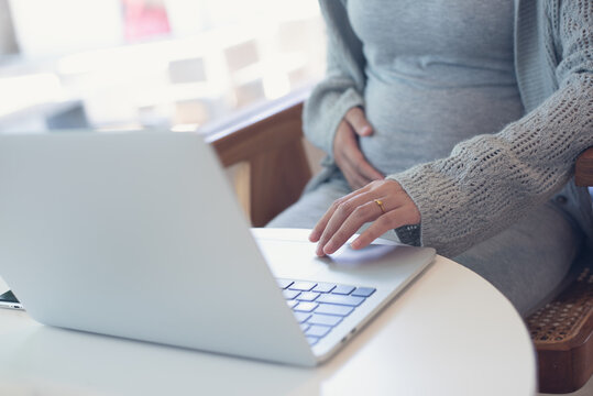 Pregnant woman working on laptop. Cropped image of pregnant businesswoman sitting at table typing on laptop at her working place in office