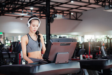 Attractive young asian woman with headphones on a treadmill in fitness sport club. Concept of...