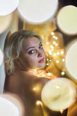 The girl is sitting in a dark room in the lights of a garland. Portrait of a middle-aged woman.