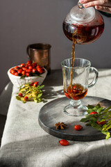 female hand pours hot herbal tea into a glass mug. Vertical
