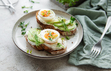 Bread toast, boiled eggs, avocado slice, microgreens on a plate