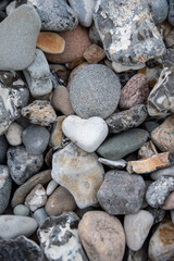 Weißer Stein in Form eines Herzens inmitten von Steinen am Strand