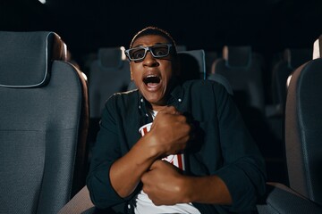 A man is watching a movie in the cinema. The emotion of fright, fear, surprise.