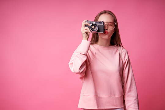 Traveler and photographer. Studio portrait of pretty young girl holding photocamera. Pink blackground.