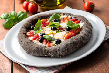 Deliziosa pizza con carbone vegetale e condita con mozzarella, pomodoro, olive, basilico e olio di...