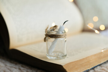 burning candle in a glass jar on the background of an old open book. Holiday bokeh lights in the background.	