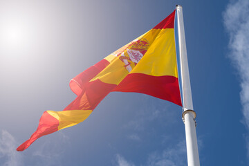 Flag of Spain with red and yellow colors waving in the wind during a sunny day with blue sky