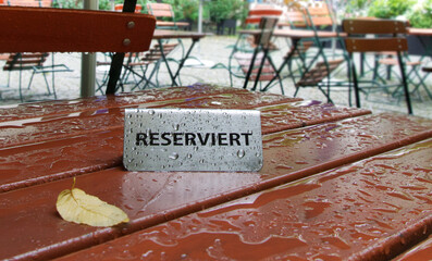 Reserviert Schild auf regennassem Tisch in einem Biergarten/Gartenlokal, horizontal 