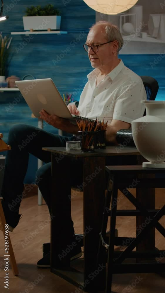 Poster vertical video: old person browsing internet to find artistic inspiration on laptop computer, using 