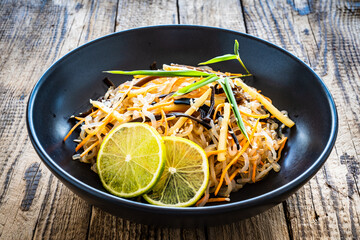 Asian food - konjac noodles, stir fried vegetables, soy sauce and mushrooms on wooden table
