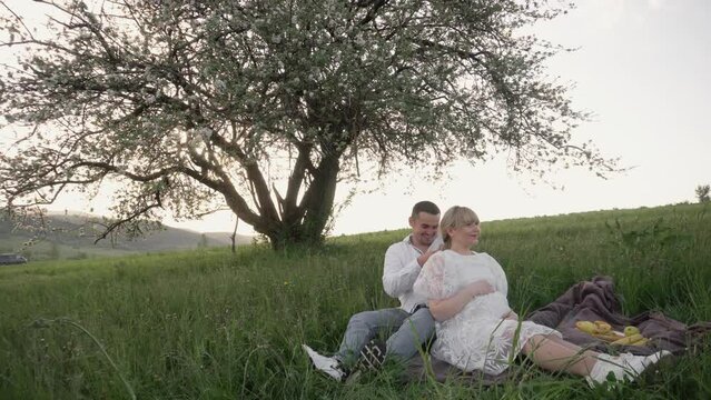 A pregnant woman and her husband are waiting for the birth of a child. Young family. A young pregnant girl and her boyfriend are relaxing in nature. Happy young couple in white shirt and dress.