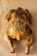 Whole chicken coated in mixed herbs roasted in an oven. On a brown paper background