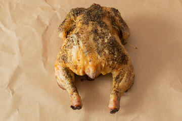 Whole chicken coated in mixed herbs roasted in an oven. On a brown paper background