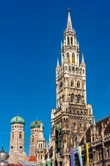 Die im Stil der Neugotik gestaltete Fassade des neuen Rathaus mit Rathausturm in der Altstadt von München in Unteransicht vom Marienplatz aus gesehen bei schönem Sommerwetter und blauen Himmel mit den