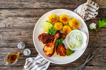 Roasted chicken drumsticks with fried potato and cucumbers in cream on wooden table

