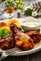 Roasted chicken drumsticks with fried potato and cucumbers in cream on wooden table

