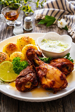 Roasted chicken drumsticks with fried potato and cucumbers in cream on wooden table

