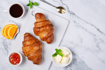 Fresh sweet croissants with butter and apricot jam for breakfast. Continental breakfast on a white concrete table. Top view with copy space. Flat lay