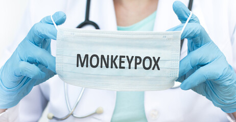 Monkeypox text on a blue protective mask in the hands of a doctor, a large hand