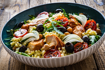 Tasty salad - fried chicken nuggets, chickpeas , bulgur groats, mini tomatoes and fresh green vegetables on wooden background
