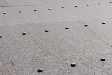 Rows of large brass rivets in the gray stone pavement. Angle view. Selective focus.