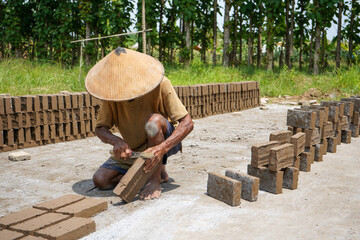 Kudus, Indonesia - September, 2022 : A male worker is making red bricks (batu bata merah) using a...