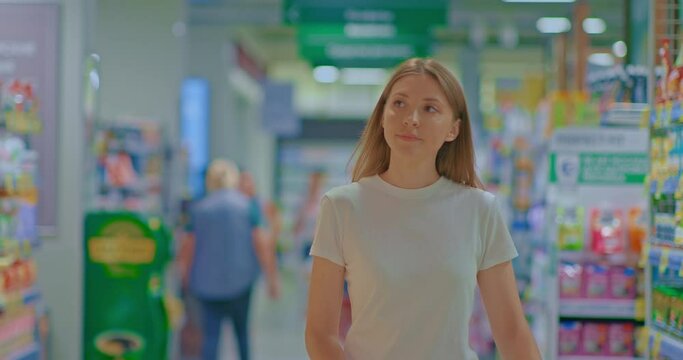 Portrait, beautiful woman walks through the supermarket and smiles. Young woman looks at the goods, shopping for groceries in the store. 4k, ProRes