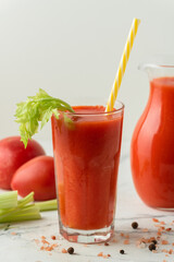 Fresh tomato juice in a glass with a straw on the white background. Red tomato juice cocktail with tomatoes and celery