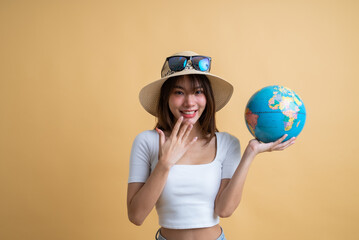 young attractive Asian woman traveler in casual clothes wearing straw hat with sunglasses holding a globe in her hands isolated on yellow background, Tourist girl having cheerful holiday trip concept