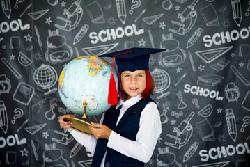  smiling  girl in academic hat and black and white uniform with globe on blackboard background in school