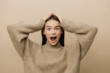 horizontal photo of an emotional, vividly expressing her emotions of a woman standing in a stylish sweater with her hands raised behind her head